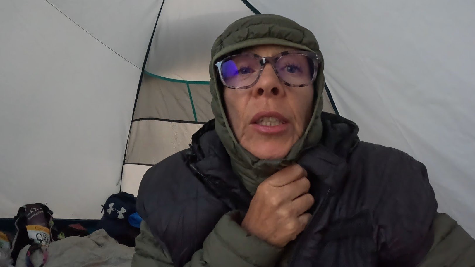 Cold and exhausted in a tent, hooded jacket pulled up, glasses on