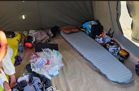 Inside a multi-stage race tent, sleeping mats laid out, kit beginning to spread